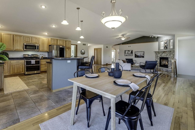 dining room with dark wood-type flooring, ceiling fan, lofted ceiling, and a stone fireplace