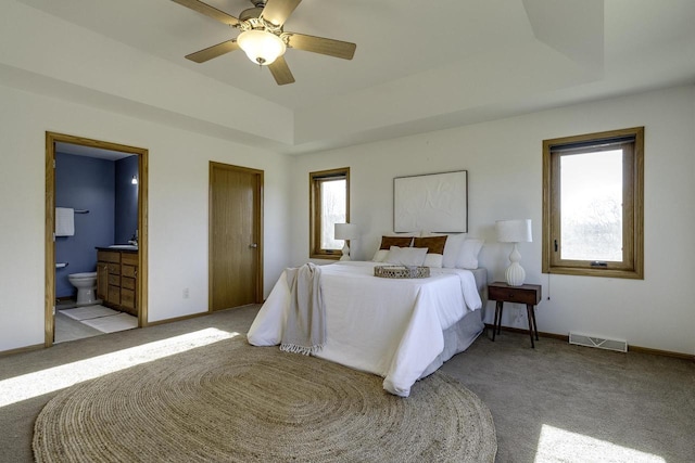 carpeted bedroom featuring ensuite bathroom, ceiling fan, and a tray ceiling