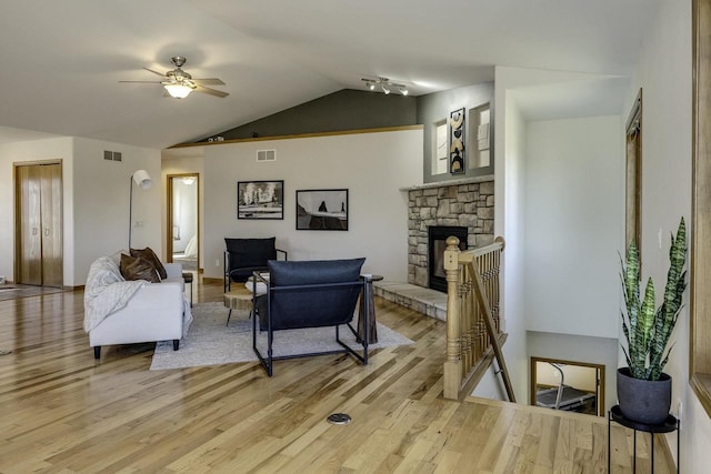 living room featuring lofted ceiling, a stone fireplace, light hardwood / wood-style flooring, and ceiling fan