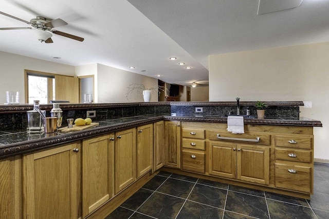 kitchen with ceiling fan, dark stone counters, and kitchen peninsula