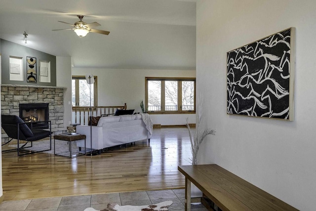 living room featuring light hardwood / wood-style flooring, a stone fireplace, vaulted ceiling, and ceiling fan