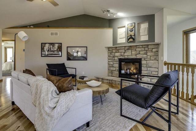 living room with ceiling fan, a fireplace, vaulted ceiling, and light hardwood / wood-style flooring