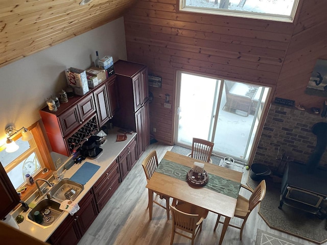 dining room with light wood-type flooring, wooden walls, sink, and a wood stove