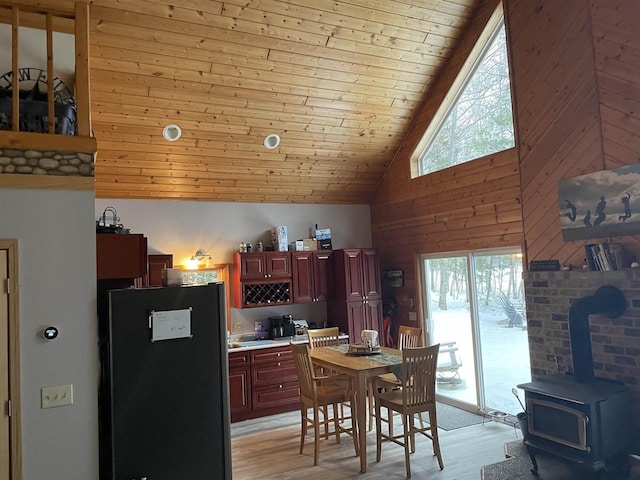 kitchen with stainless steel fridge, wooden walls, high vaulted ceiling, wooden ceiling, and light wood-type flooring