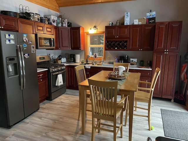 kitchen with light wood-type flooring, vaulted ceiling, and appliances with stainless steel finishes