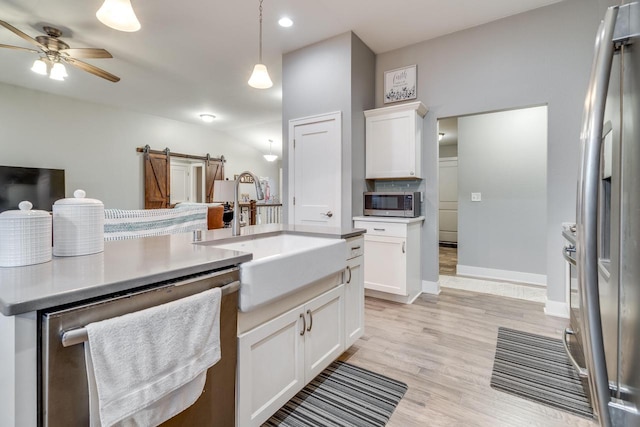 kitchen with stainless steel appliances, a barn door, decorative light fixtures, and white cabinets