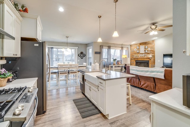 kitchen featuring light hardwood / wood-style floors, gas stove, an island with sink, white cabinets, and decorative light fixtures