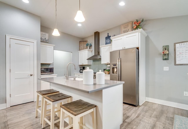 kitchen with appliances with stainless steel finishes, sink, white cabinets, hanging light fixtures, and wall chimney range hood