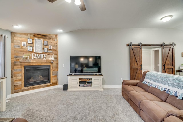 carpeted living room with vaulted ceiling, a barn door, a stone fireplace, and ceiling fan