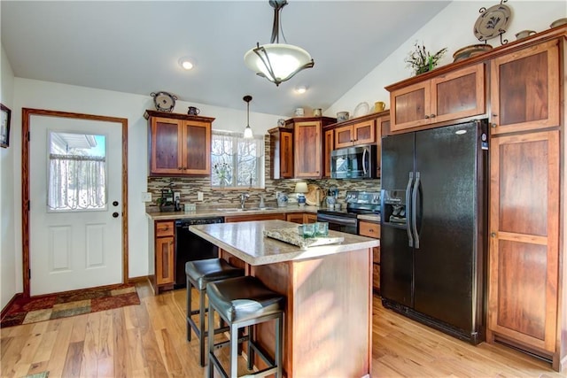 kitchen featuring sink, decorative light fixtures, a center island, light hardwood / wood-style flooring, and black appliances