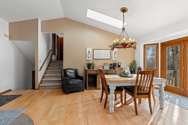 dining area featuring an inviting chandelier, vaulted ceiling with skylight, and hardwood / wood-style floors