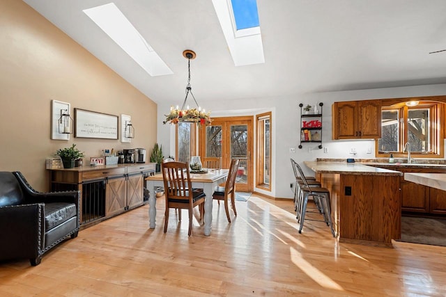 dining space featuring an inviting chandelier, sink, light hardwood / wood-style flooring, and vaulted ceiling with skylight