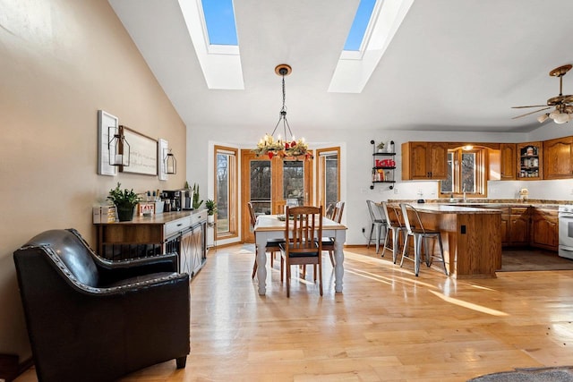 dining space with sink, lofted ceiling with skylight, ceiling fan with notable chandelier, and light hardwood / wood-style flooring