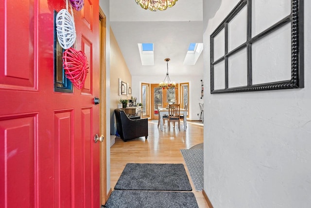 entrance foyer with vaulted ceiling with skylight, a notable chandelier, and light hardwood / wood-style flooring