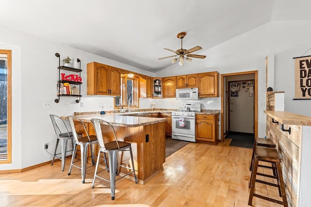 kitchen featuring a breakfast bar area, vaulted ceiling, kitchen peninsula, white appliances, and light hardwood / wood-style floors