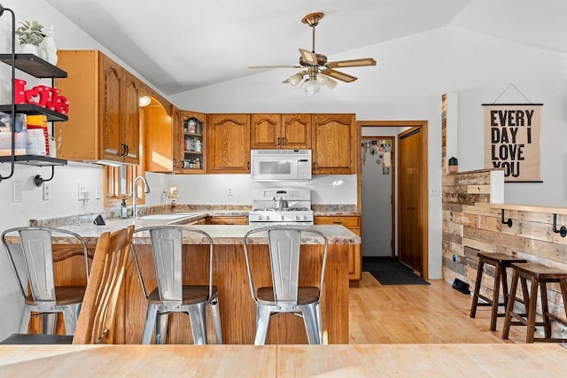 kitchen featuring lofted ceiling, sink, a breakfast bar area, kitchen peninsula, and white appliances