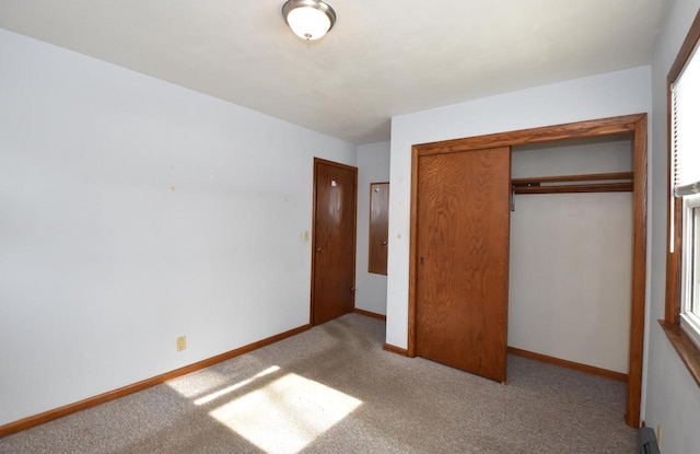 unfurnished bedroom featuring a baseboard radiator, light colored carpet, and a closet