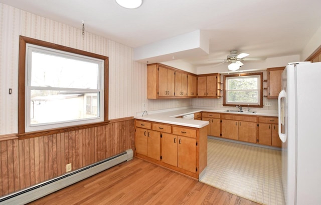 kitchen featuring sink, white fridge, a baseboard heating unit, light hardwood / wood-style floors, and kitchen peninsula