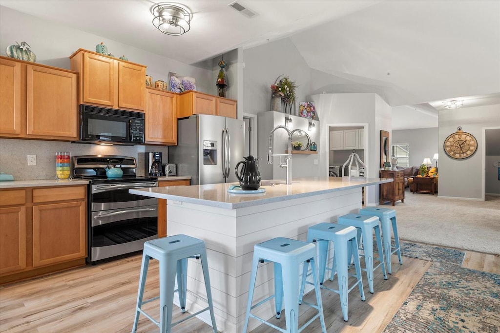 kitchen featuring vaulted ceiling, appliances with stainless steel finishes, a breakfast bar area, and light hardwood / wood-style floors