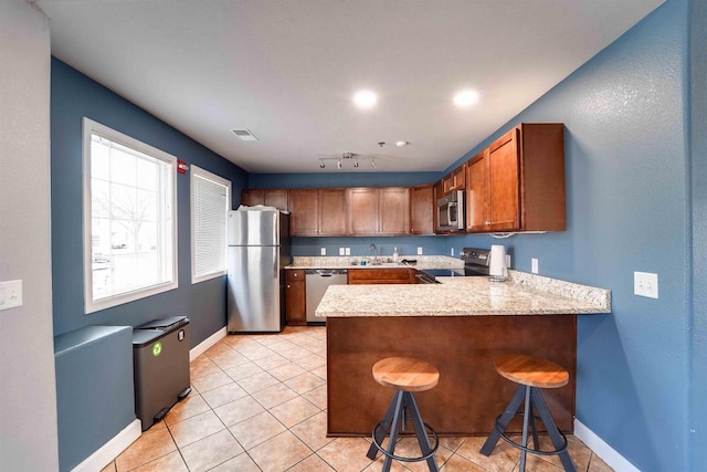 kitchen with sink, light tile patterned floors, appliances with stainless steel finishes, a kitchen breakfast bar, and kitchen peninsula