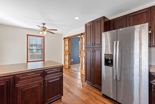 kitchen featuring ceiling fan, a barn door, stainless steel fridge with ice dispenser, and light hardwood / wood-style flooring