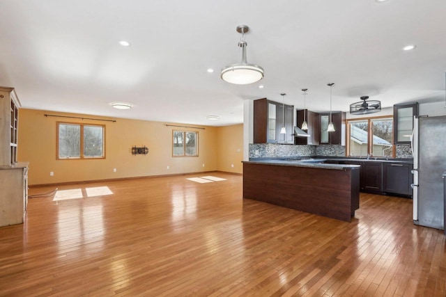 8209 N Port Washington Rd, Fox Point, WI 53217 - kitchen featuring dark brown cabinetry, decorative backsplash, open floor plan, freestanding refrigerator, and wall chimney range hood