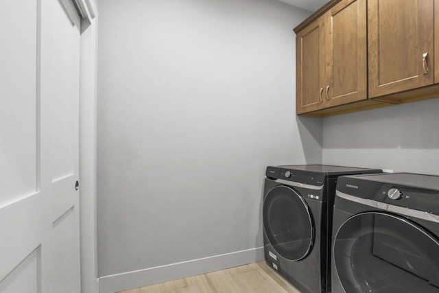 clothes washing area featuring cabinets, separate washer and dryer, and light hardwood / wood-style flooring