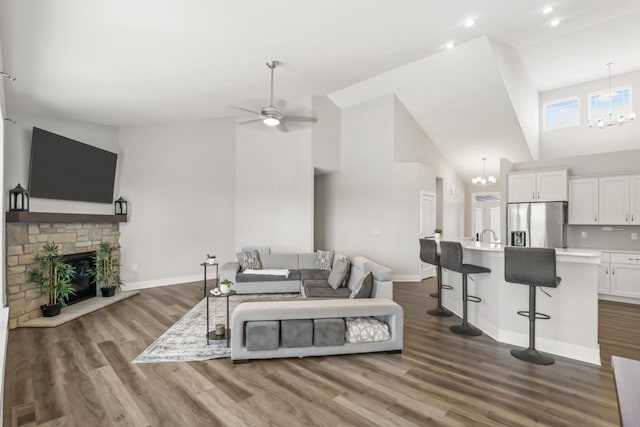 living room with high vaulted ceiling, wood-type flooring, a fireplace, and ceiling fan with notable chandelier