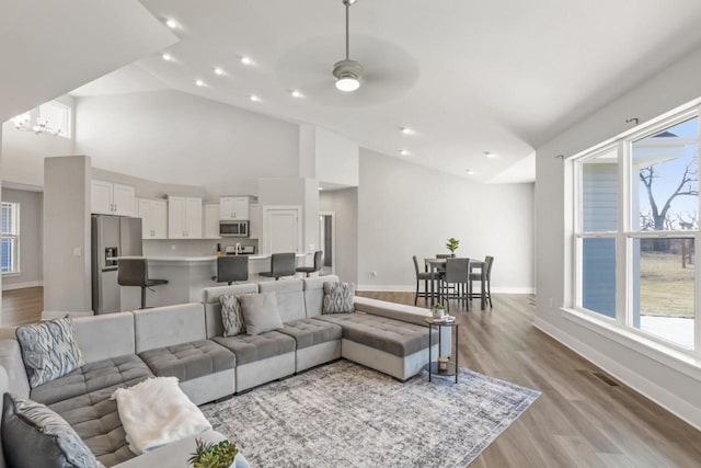 living room with ceiling fan, high vaulted ceiling, and light wood-type flooring