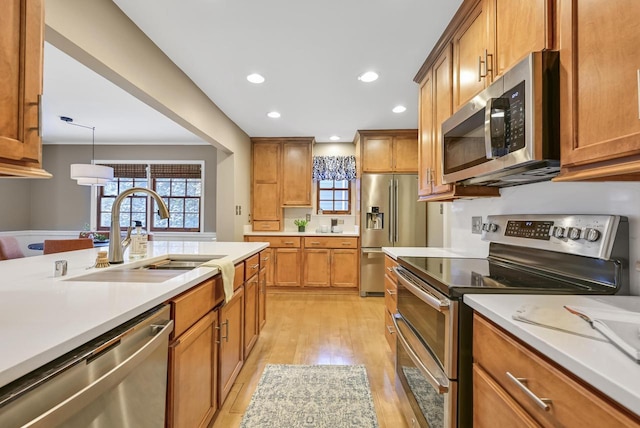 kitchen featuring appliances with stainless steel finishes, sink, light hardwood / wood-style floors, and decorative light fixtures