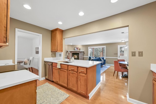 kitchen featuring sink, light wood-type flooring, stainless steel dishwasher, kitchen peninsula, and a fireplace