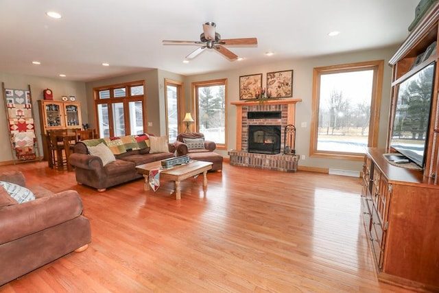 living room with a fireplace, ceiling fan, and light wood-type flooring