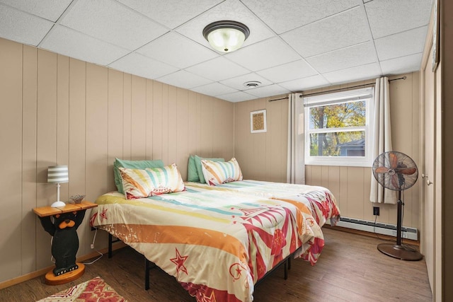 bedroom with wood-type flooring, a baseboard heating unit, and a paneled ceiling