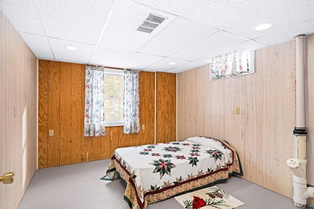 bedroom with a paneled ceiling, concrete flooring, and wood walls