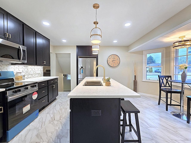 kitchen with sink, a kitchen island with sink, hanging light fixtures, stainless steel appliances, and a kitchen breakfast bar