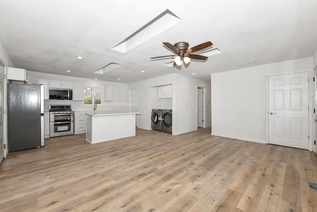 kitchen with a center island, a skylight, appliances with stainless steel finishes, washer and clothes dryer, and white cabinets