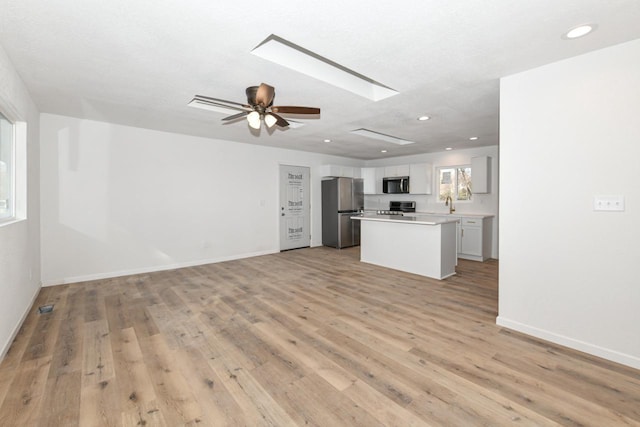 unfurnished living room featuring ceiling fan, sink, light wood-type flooring, and a skylight