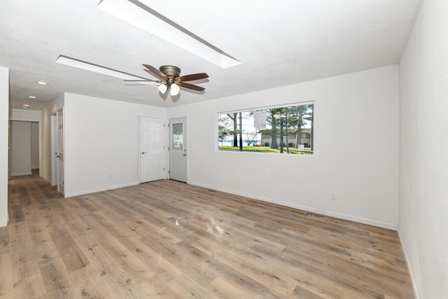 spare room featuring ceiling fan, a textured ceiling, light hardwood / wood-style floors, and a skylight