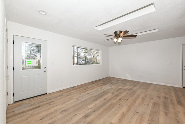 foyer entrance featuring ceiling fan, a skylight, light hardwood / wood-style floors, and a textured ceiling