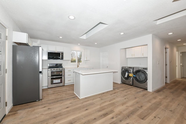 kitchen featuring white cabinetry, a skylight, appliances with stainless steel finishes, a kitchen island, and independent washer and dryer