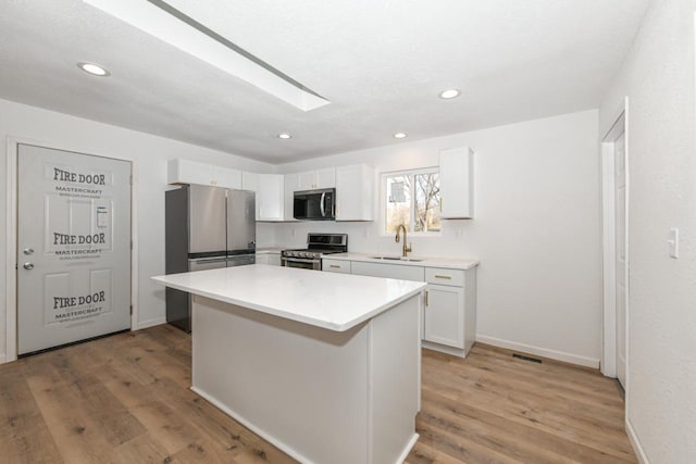 kitchen featuring sink, a skylight, a center island, stainless steel appliances, and white cabinets