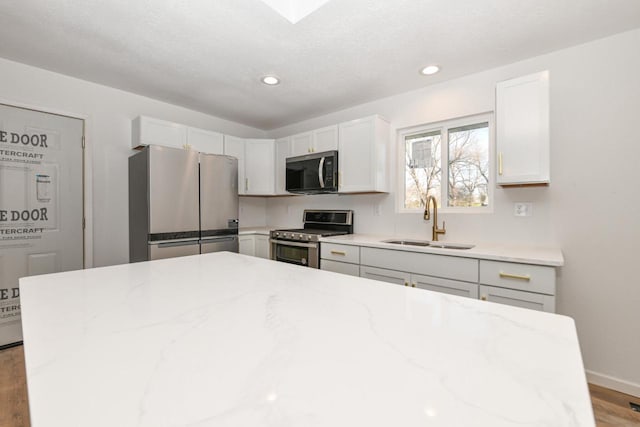 kitchen featuring sink, light hardwood / wood-style flooring, stainless steel appliances, light stone counters, and white cabinets