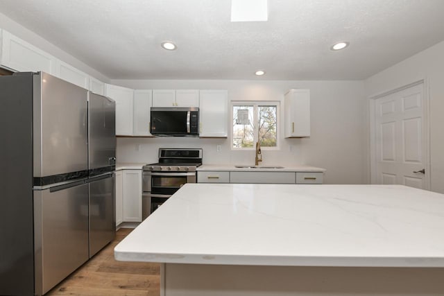 kitchen with sink, appliances with stainless steel finishes, white cabinetry, light stone counters, and light hardwood / wood-style floors