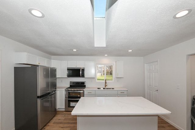 kitchen featuring sink, white cabinetry, stainless steel appliances, light stone countertops, and a kitchen island