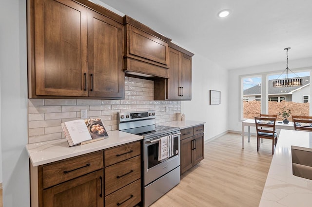 kitchen with decorative light fixtures, tasteful backsplash, stainless steel range with electric cooktop, light hardwood / wood-style floors, and light stone counters