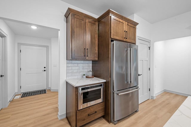 kitchen with light stone counters, high end refrigerator, light wood-style flooring, and decorative backsplash