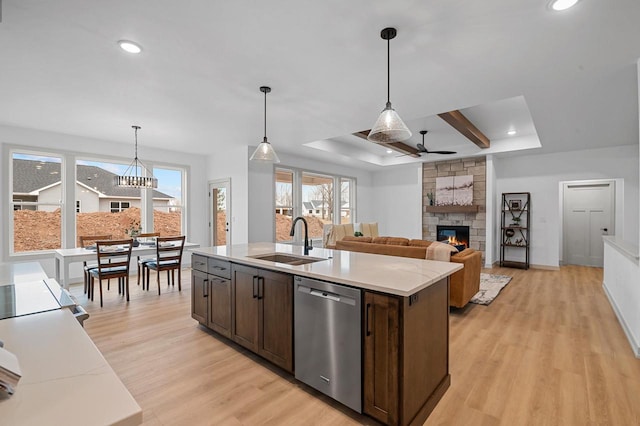 kitchen with light wood-style flooring, a tray ceiling, dark brown cabinets, stainless steel dishwasher, and a sink