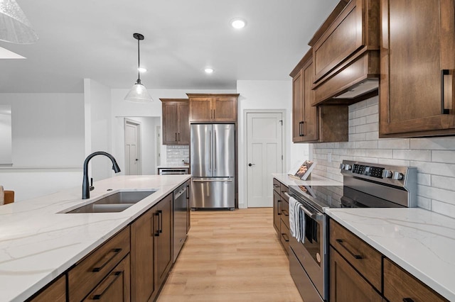 kitchen with light stone counters, stainless steel appliances, light wood-style floors, pendant lighting, and a sink