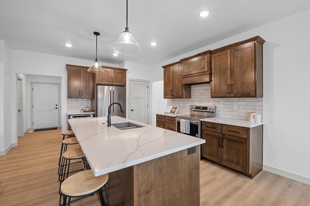 kitchen featuring pendant lighting, stainless steel appliances, a sink, light wood-type flooring, and a kitchen breakfast bar