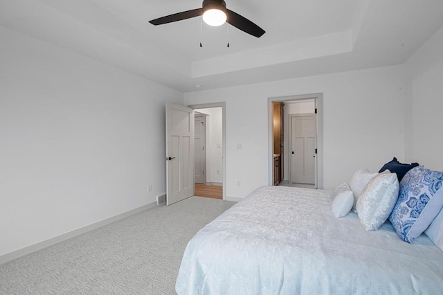 carpeted bedroom with a raised ceiling and ceiling fan